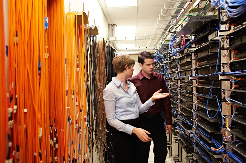 One IT worker assessing another in server room.