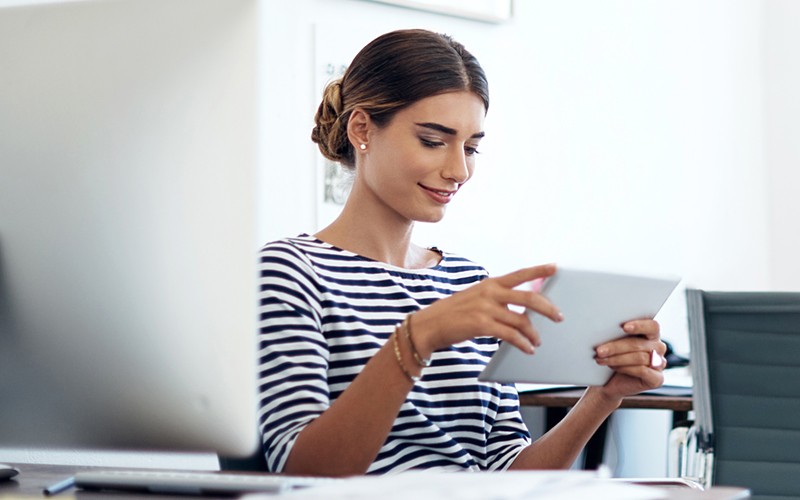 Smiling businesswoman on tablet device near computer enjoying seamless data integration