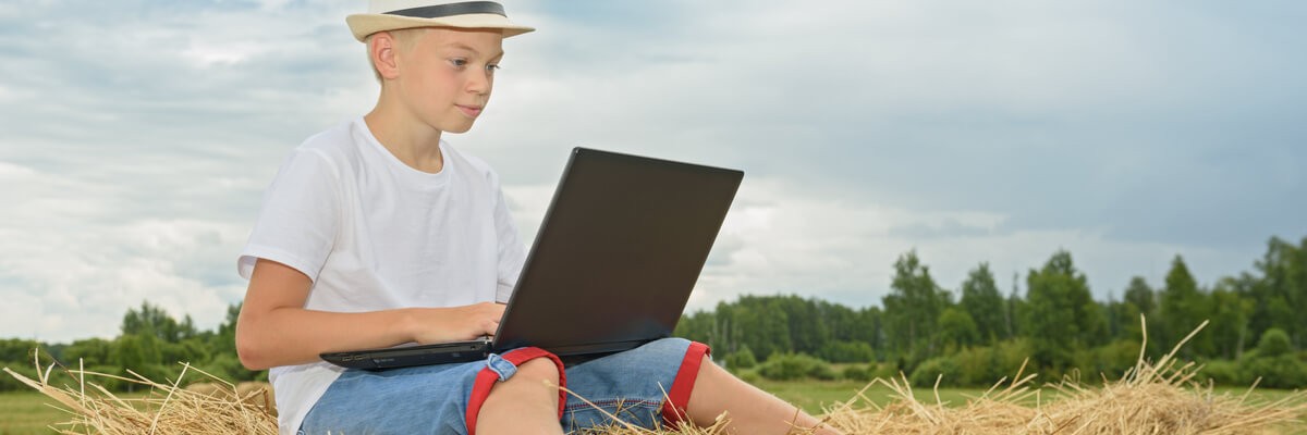 Boy using a laptop sits on hay