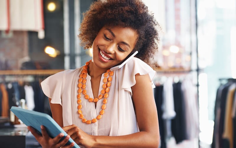 Smiling businesswoman on phone working on tablet device in retail clothing store