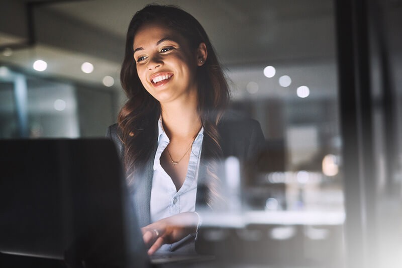 Smiling businesswoman on laptop computer in office at night