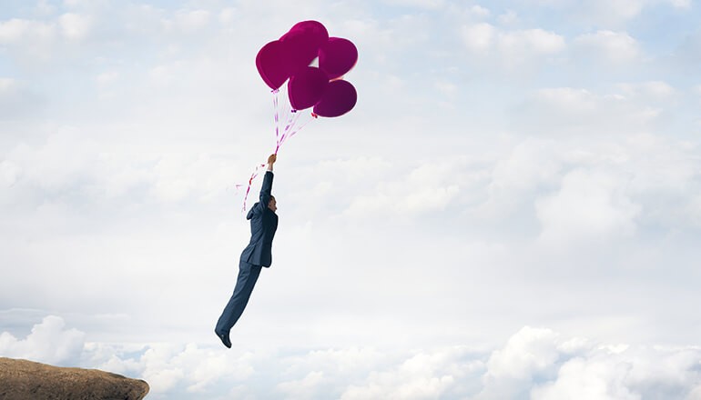 Conceptual image of a businessman holding on to balloons as he floats into clouds