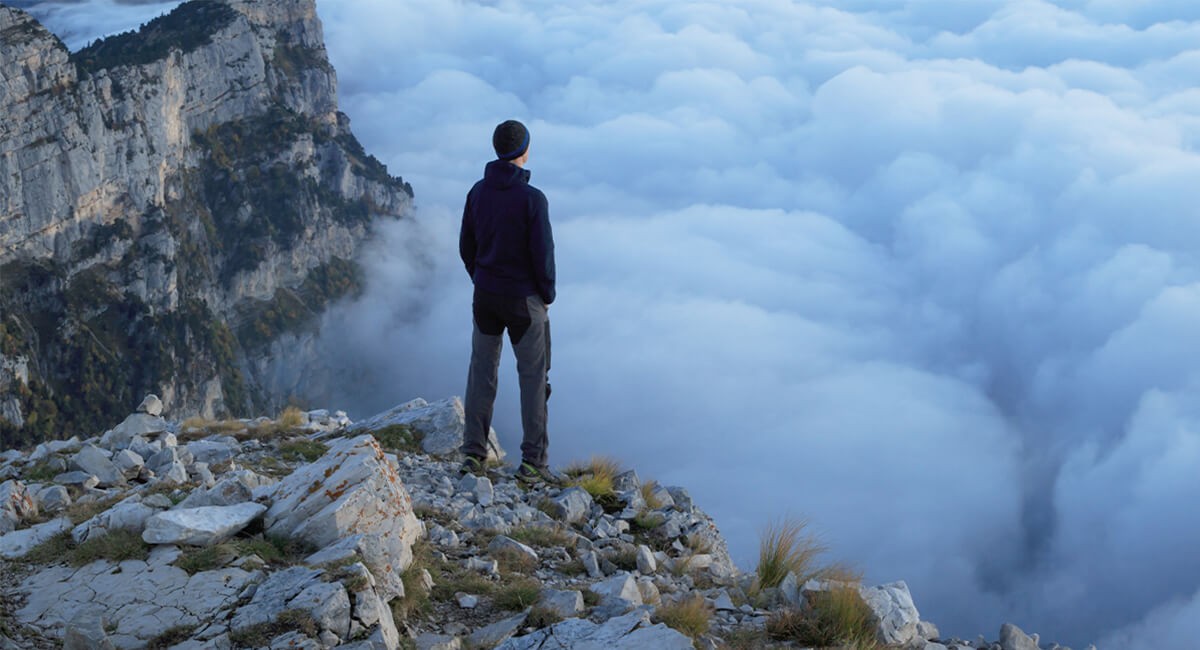 Man overlooking clouds at the peak of a mountain
