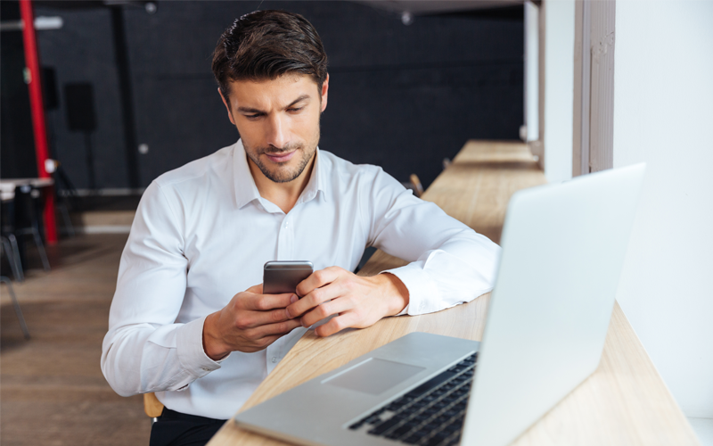 Business man holding mobile device in front of laptop