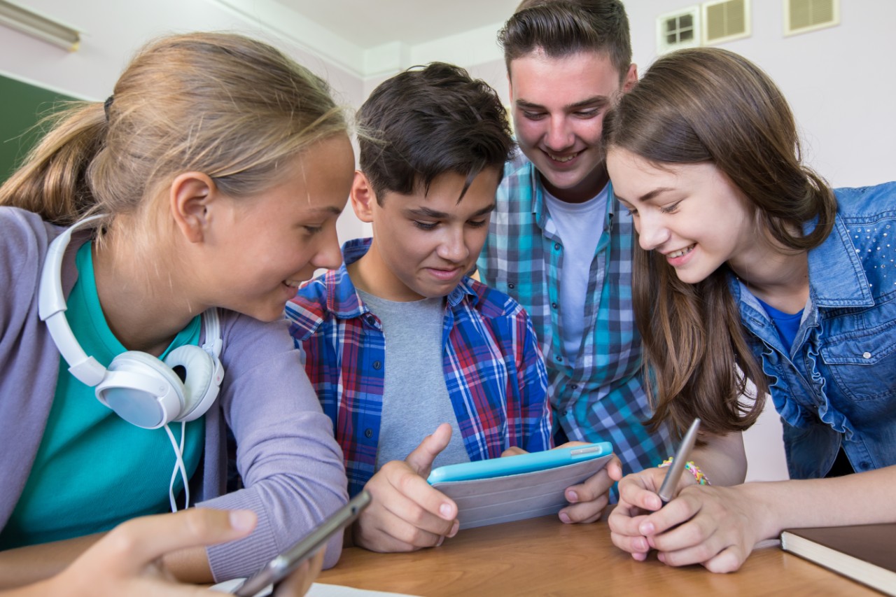Male teacher with three students looking at mobile device