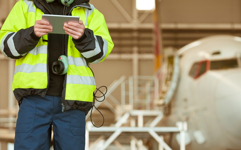 Aircraft engineer uses tablet device in front of airplane in hangar 